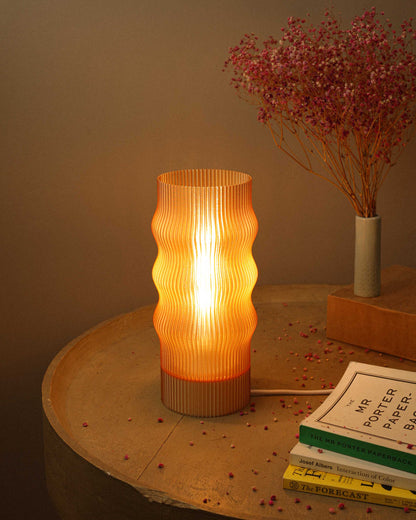 Decorative table lamp with ribbed design on a wooden surface with books and dried flowers.