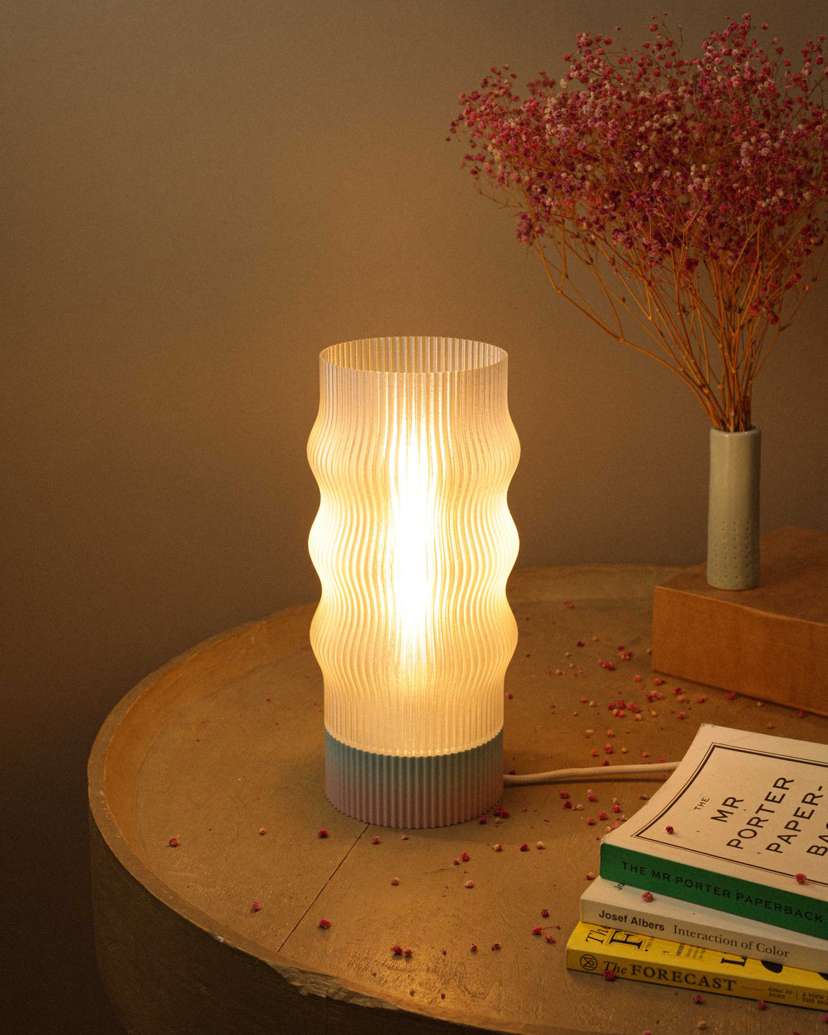Table lamp with ribbed design on a wooden surface with books and dried flowers.