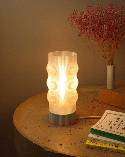 Table lamp with ribbed design on a wooden surface with books and dried flowers.