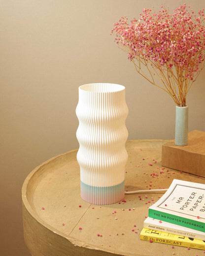 White textured vase on a wooden surface with pink flowers and books in the background