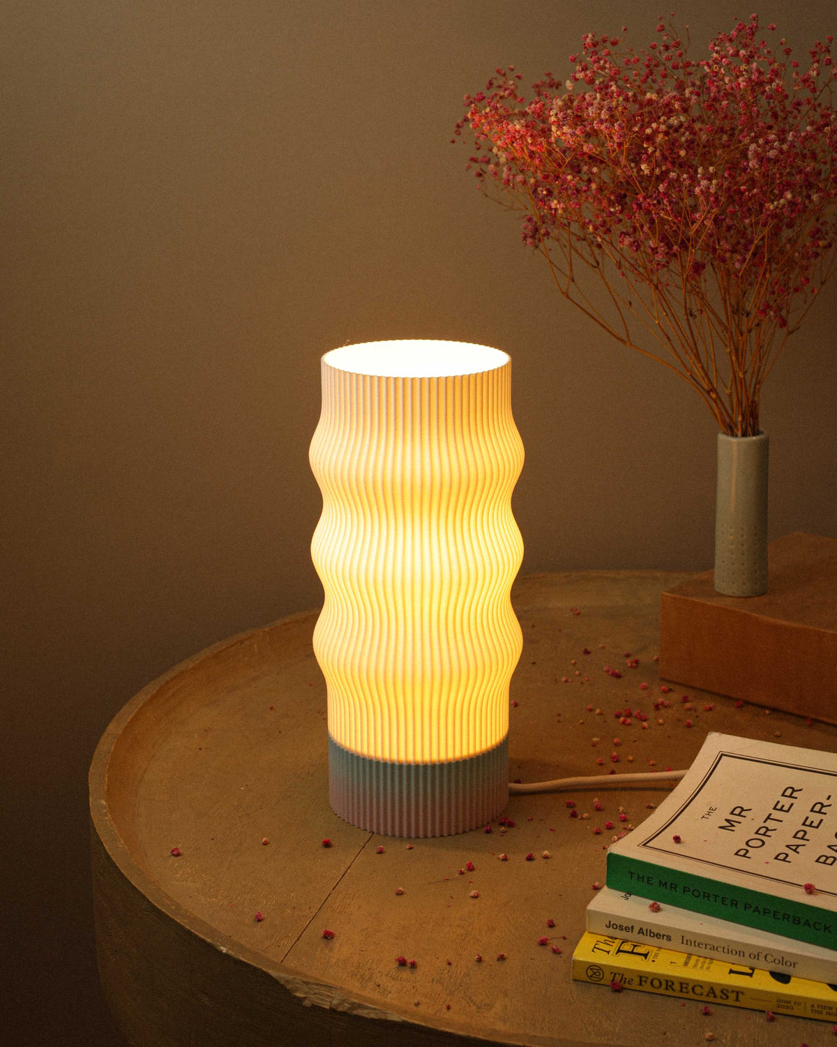 Table lamp with ribbed design on a wooden surface with books and dried flowers.