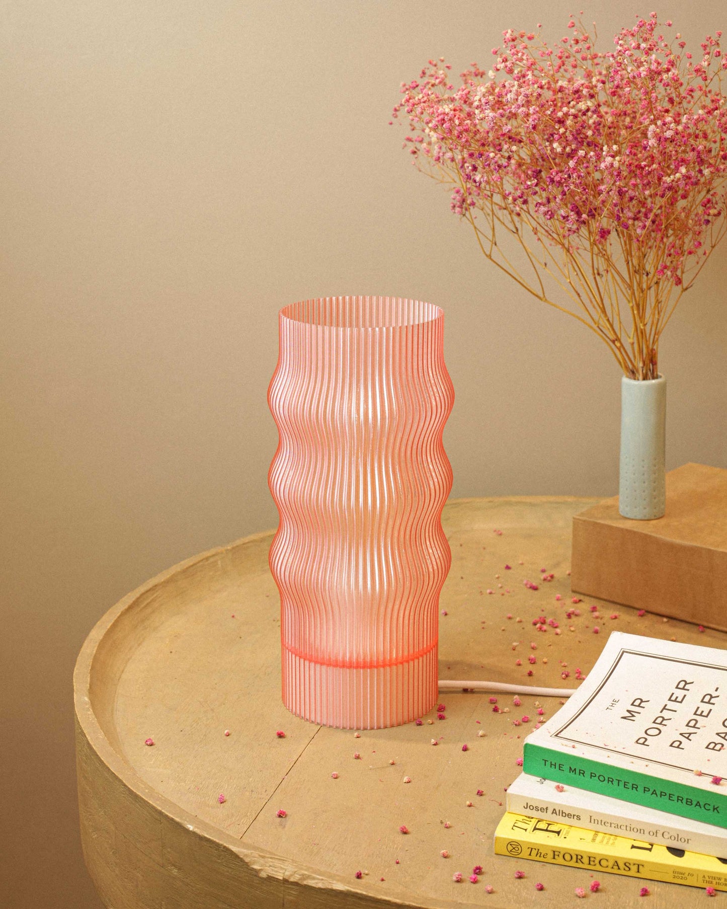 Pink textured table lamp on a wooden surface with books and flowers in the background