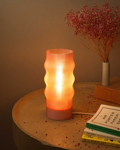 Decorative table lamp with ribbed design on a wooden surface with books and dried flowers.