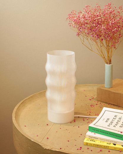 White textured table lamp on a wooden surface with books and a small plant.