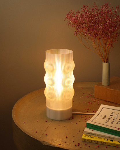 White textured table lamp on a wooden surface with books and dried flowers in the background