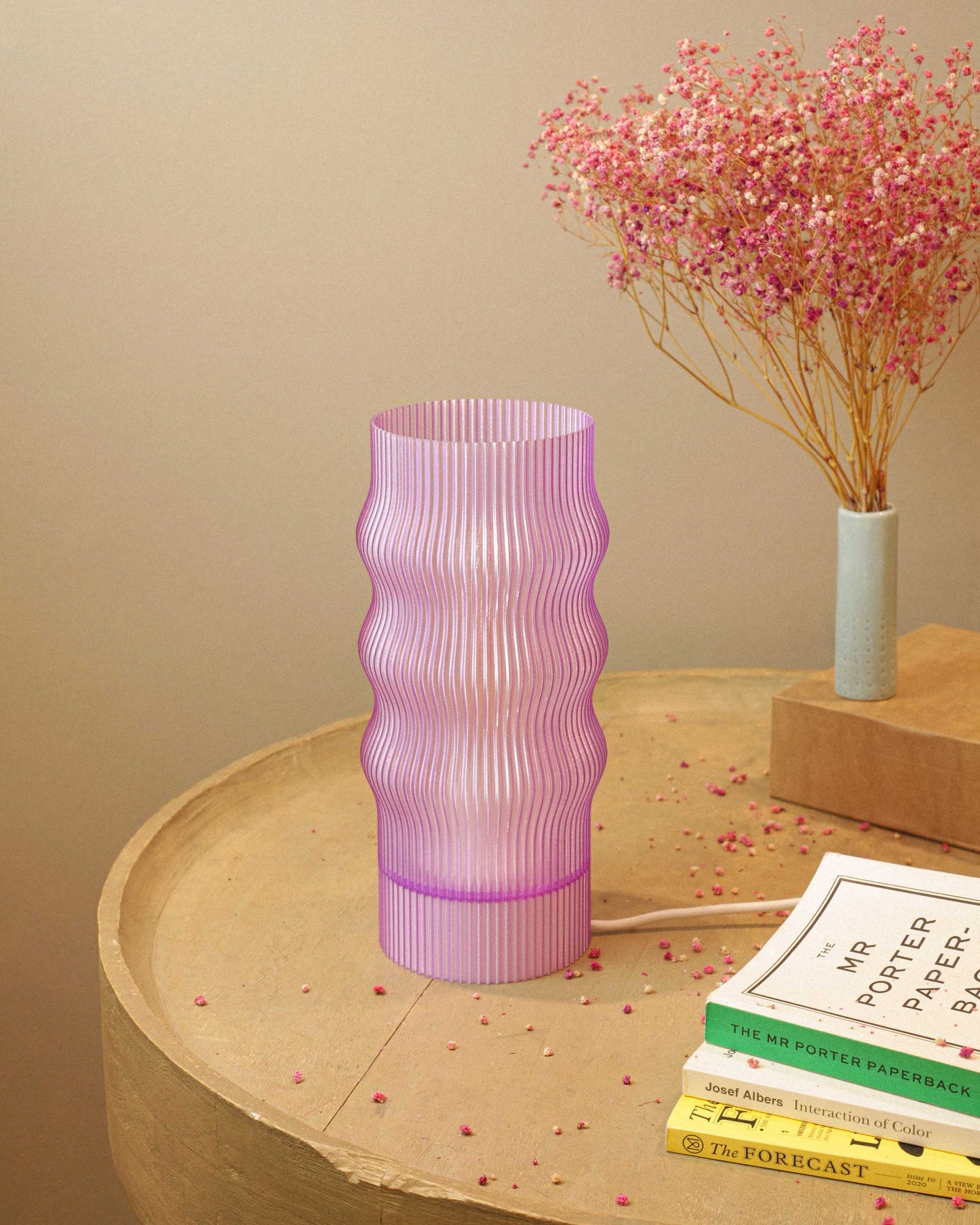 Lavender ribbed table lamp on a wooden surface with books and a small plant in the background.