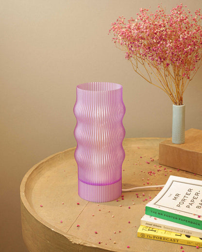 Lavender ribbed table lamp on a wooden surface with books and a small plant in the background.