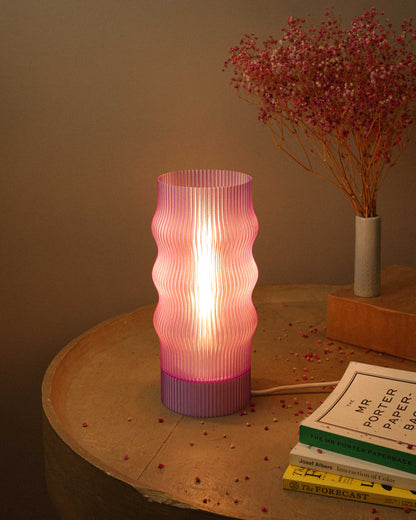 Lavender ribbed table lamp on a wooden surface with books and a vase in the background