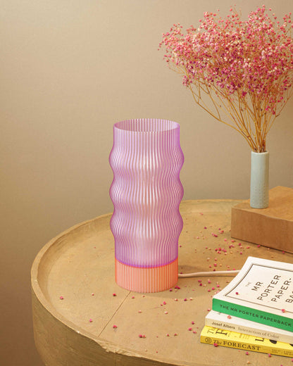 Pink ribbed table lamp on a wooden surface with books and dried flowers in the background.