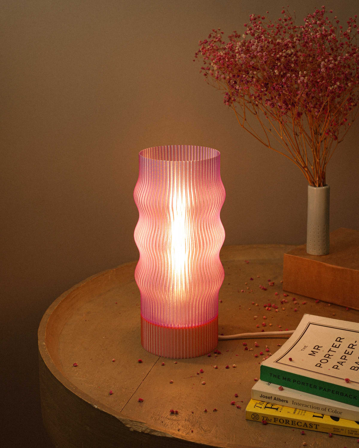 Pink textured table lamp on a wooden surface with books and dried flowers.