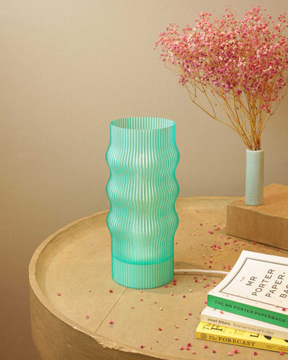 Green ribbed table lamp on a wooden surface with books and pink flowers in the background