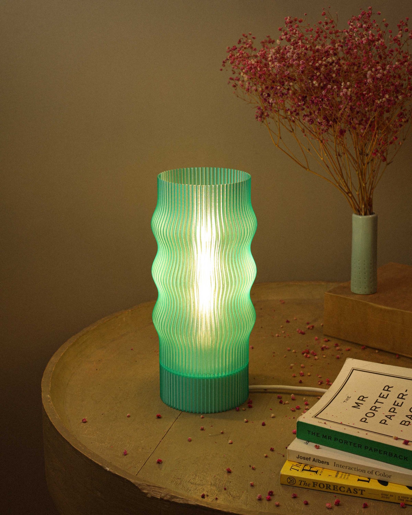 Green textured table lamp on a wooden surface with books and dried flowers.