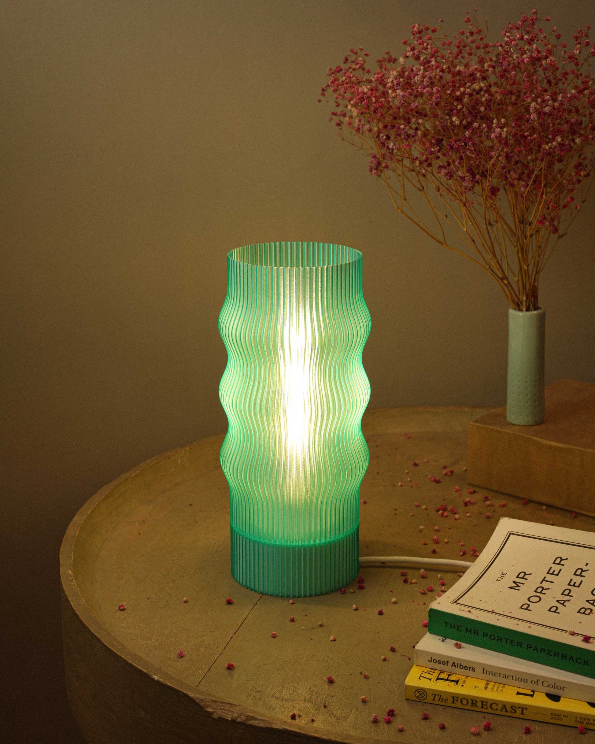 Green textured table lamp on a wooden surface with books and dried flowers.
