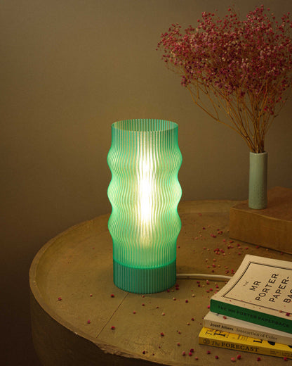 Green textured table lamp on a wooden surface with books and dried flowers.