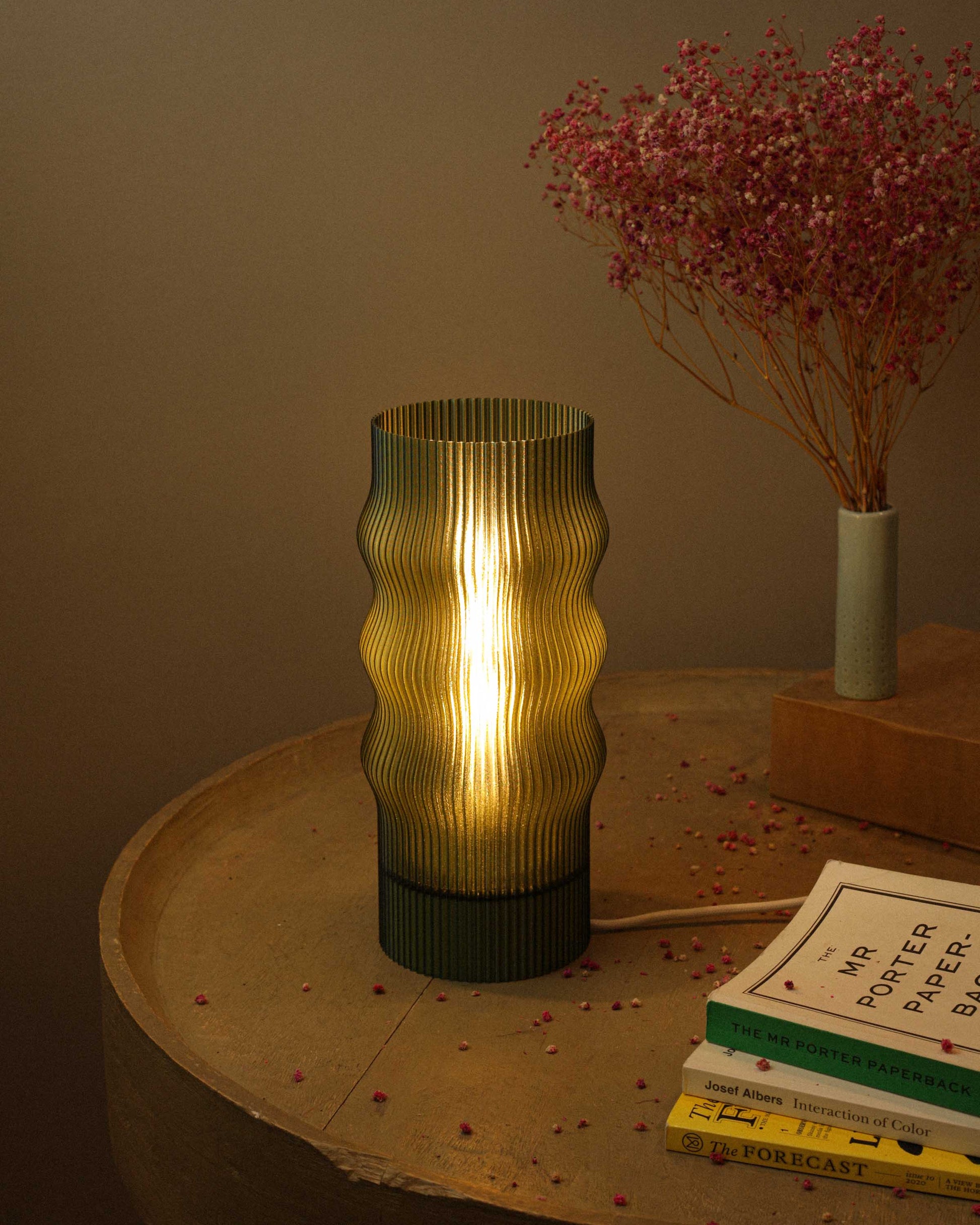 Decorative table lamp with ribbed design on a wooden surface with books and a vase in the background.