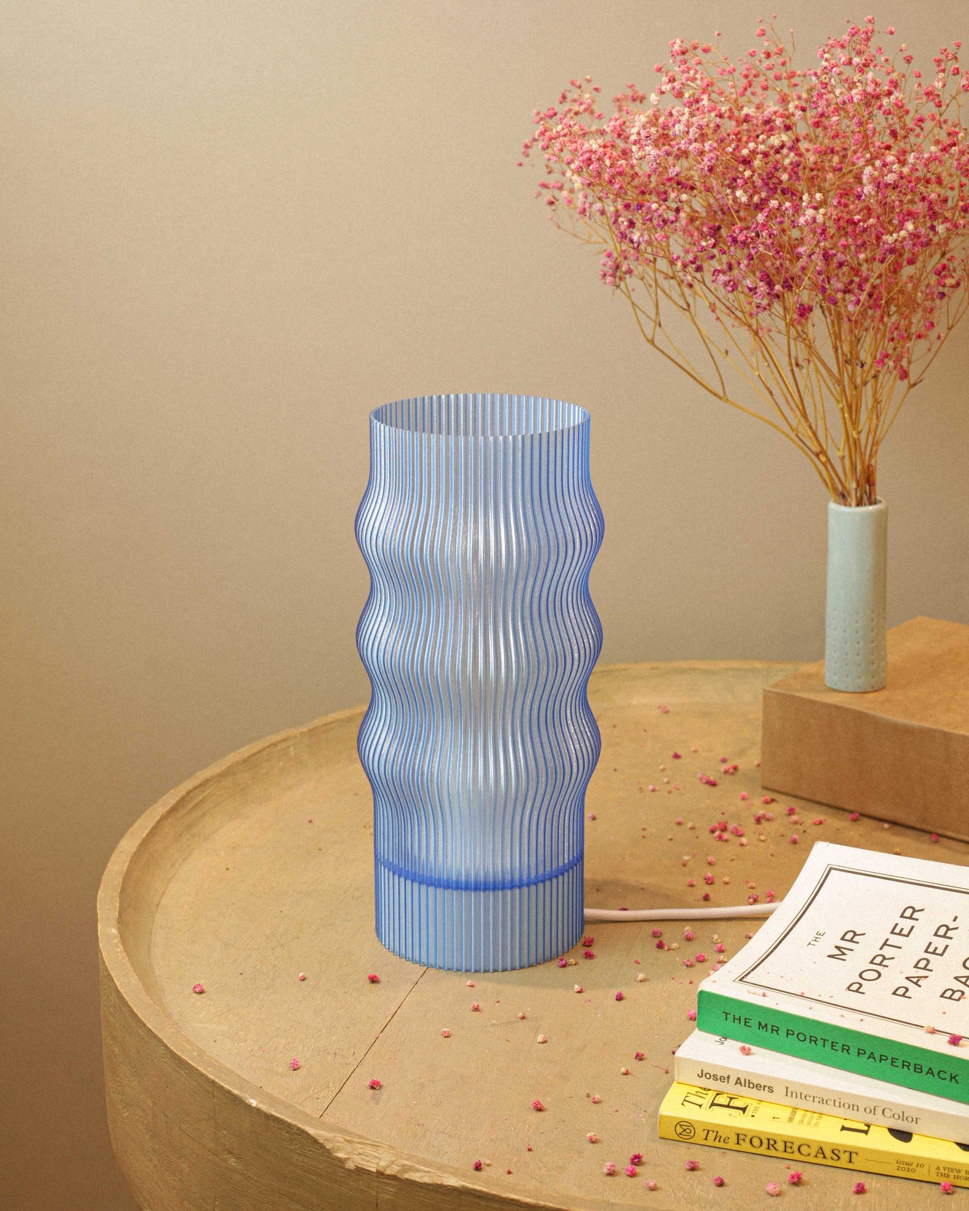 Blue textured table lamp on a wooden surface with books and a small plant in the background.