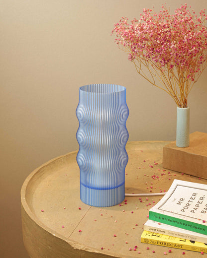Blue textured table lamp on a wooden surface with books and a small plant in the background.