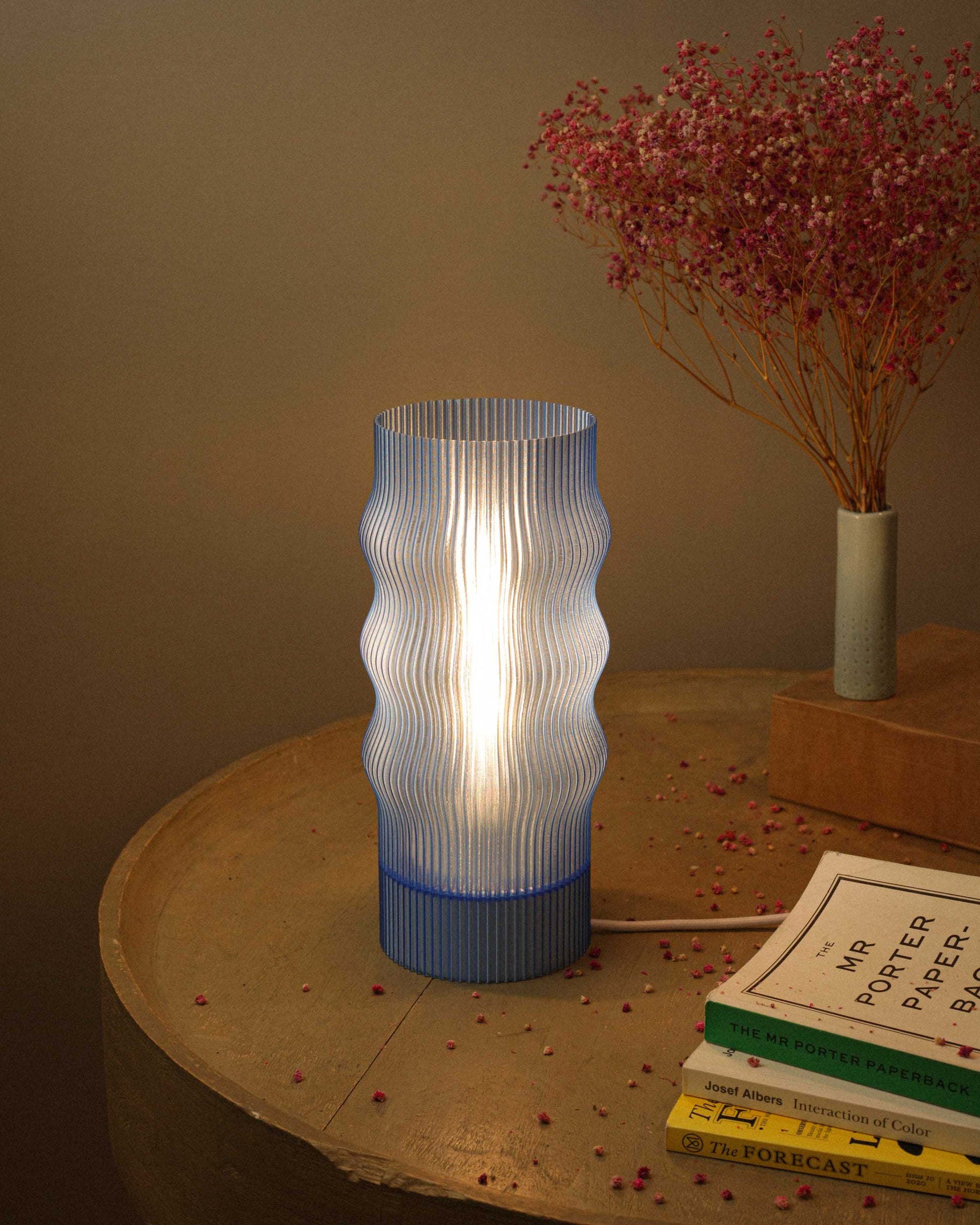 Modern table lamp with ribbed design on a wooden surface with books and dried flowers.