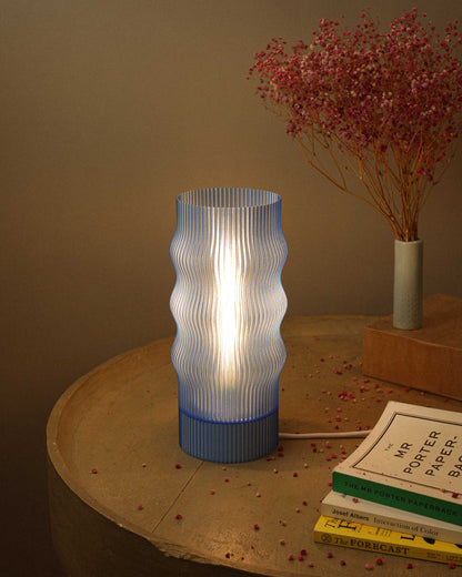 Modern table lamp with ribbed design on a wooden surface with books and dried flowers.