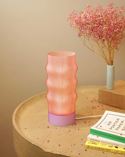 Pink textured table lamp on a wooden surface with books and a small plant.