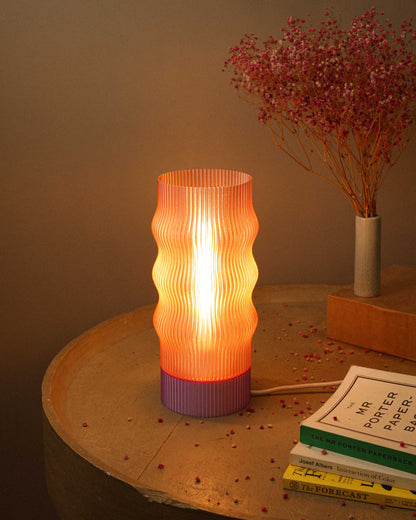 Decorative table lamp with ribbed design on a wooden surface with books and dried flowers.