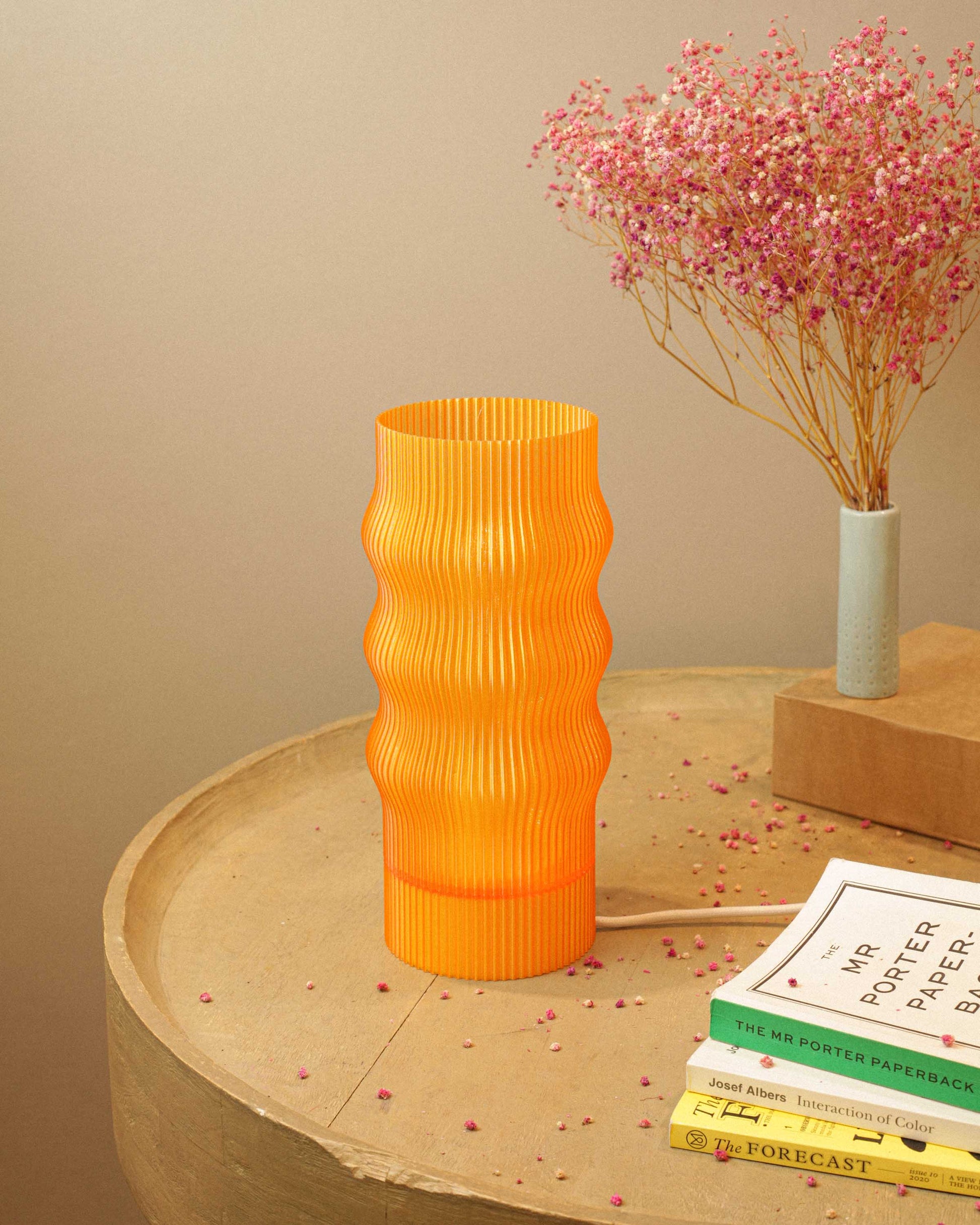 Orange textured table lamp on a wooden surface with books and a small plant in the background.