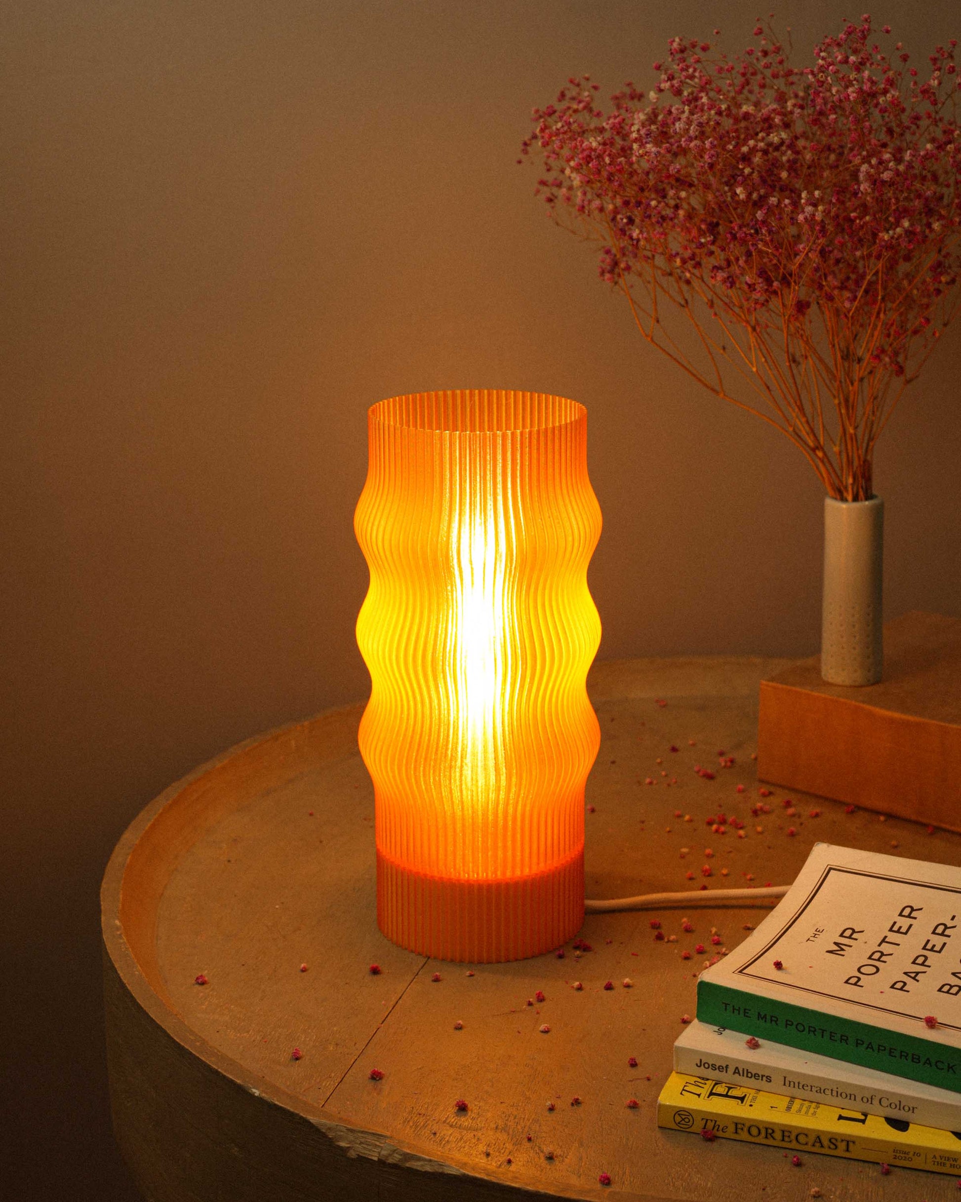 Decorative lamp with ribbed design on a table with books and dried flowers.